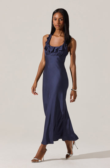 A woman is wearing a long, navy blue satin dress with ruffled straps and a fitted bodice. She has paired the dress with open-toe high-heeled shoes.