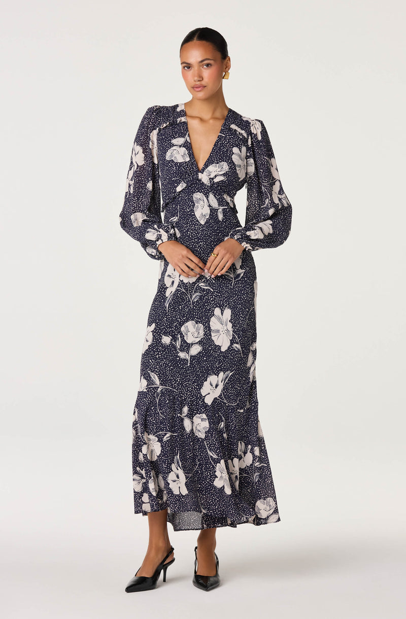 Woman in a navy blue floral long dress with white flowers, long sleeves, and a V-neck.