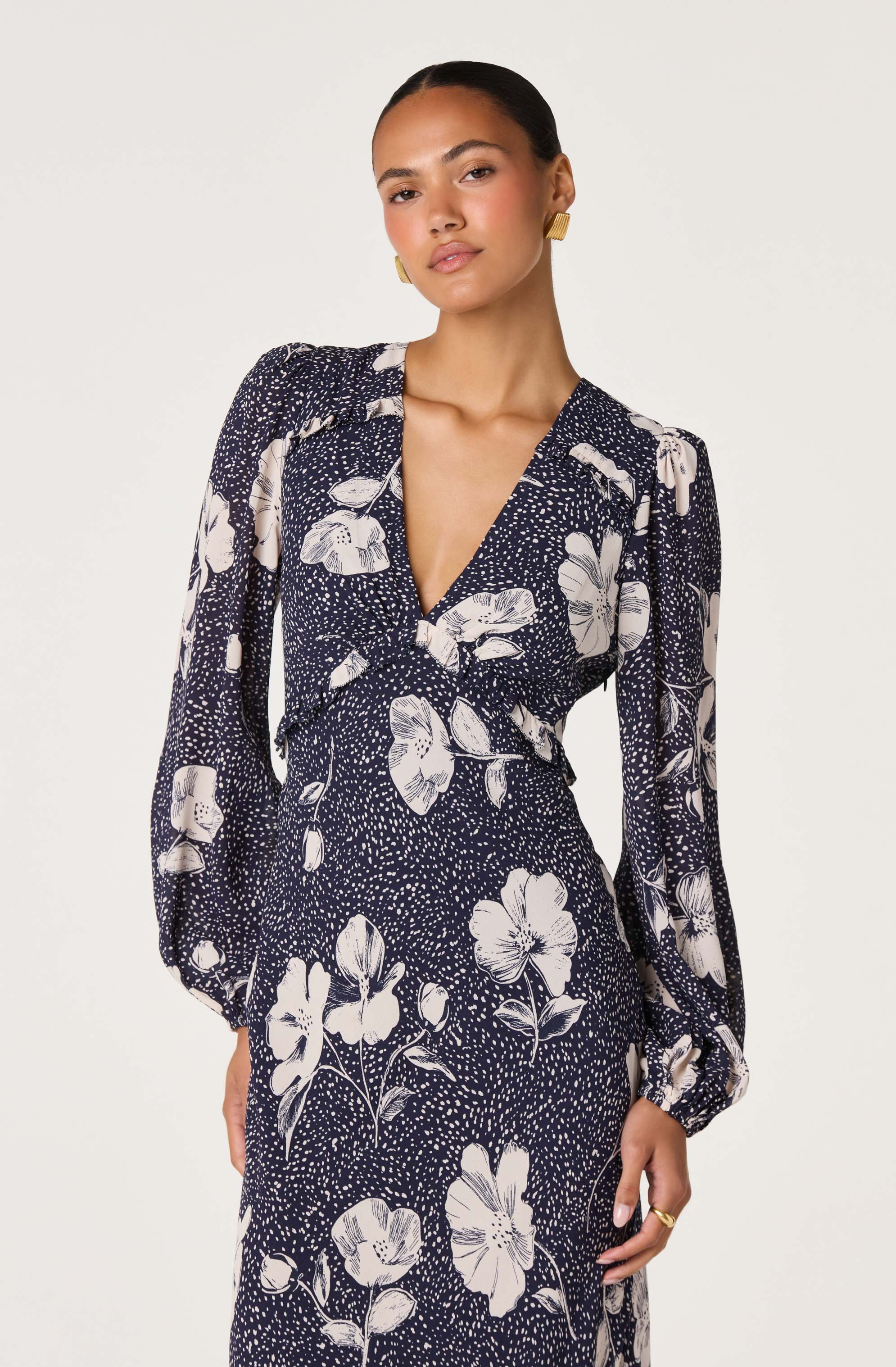 Woman wearing a navy blue dress with white floral patterns and long, puffed sleeves.
