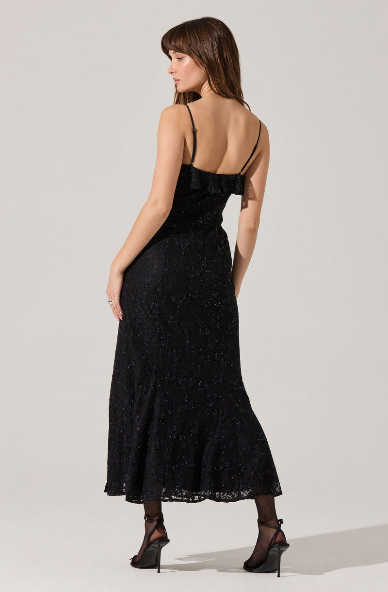 A woman is wearing a black, spaghetti strap dress with a fitted bodice and a long, flowing skirt. The dress features a subtle shimmer or sparkle throughout. She is also wearing sheer black stockings and high-heeled shoes with ankle straps.