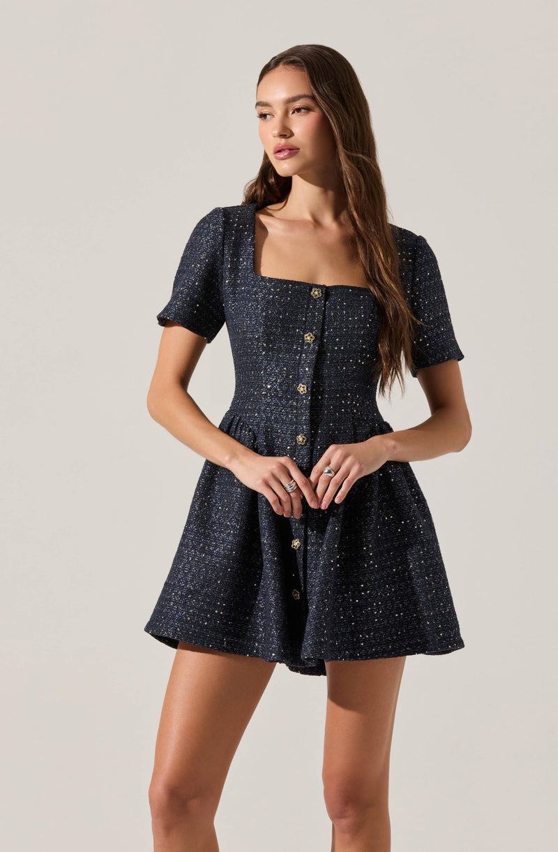 A woman is wearing a dark navy, textured, sparkly short-sleeved dress with a square neckline and a row of buttons down the front. The dress has a fitted waist and a flared skirt.
