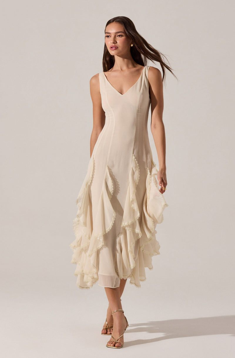 The dress is sleeveless with wide shoulder straps and a V-shaped neckline. It is made of a light, flowing fabric in an off-white or cream color. The dress features vertical seam lines on the bodice and has a layered, ruffled skirt with textured, scalloped edges, creating a tiered effect that extends to mid-calf length. The overall style is elegant and feminine.