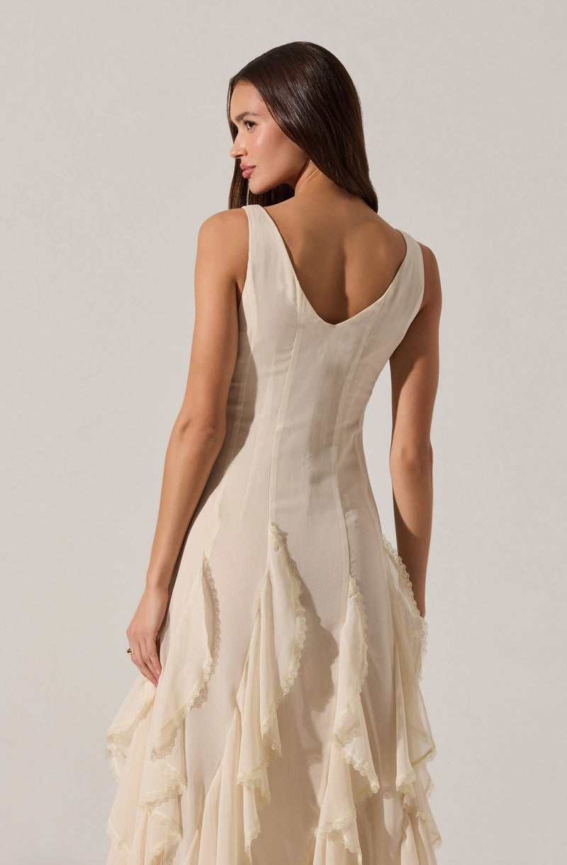 A woman is wearing an elegant, sleeveless, cream-colored dress with a fitted bodice that has vertical seams and a deep, scooped back. The skirt features layered, ruffled fabric with a slightly frayed edge, creating a textured and flowing appearance.