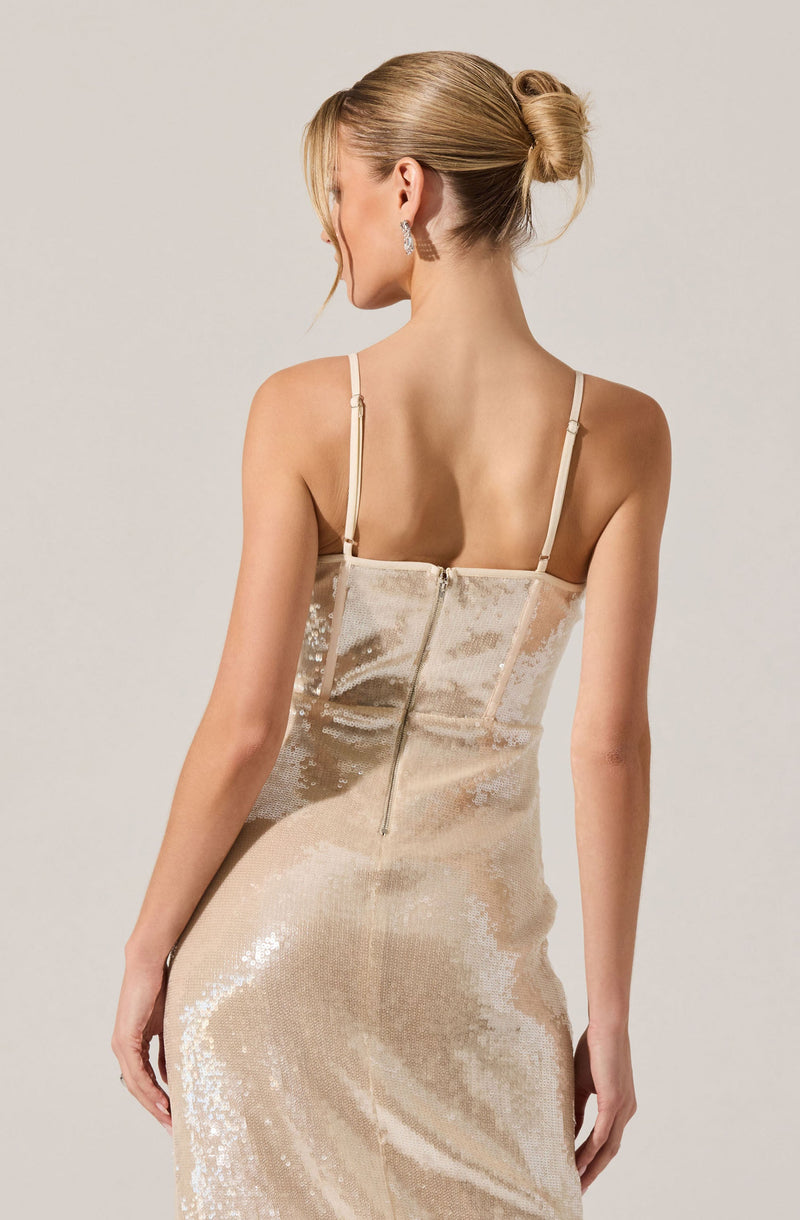 A woman is wearing a fitted, sleeveless, floor-length gown made of shimmering, light-colored sequined fabric. The dress features thin spaghetti straps and a center back zipper.