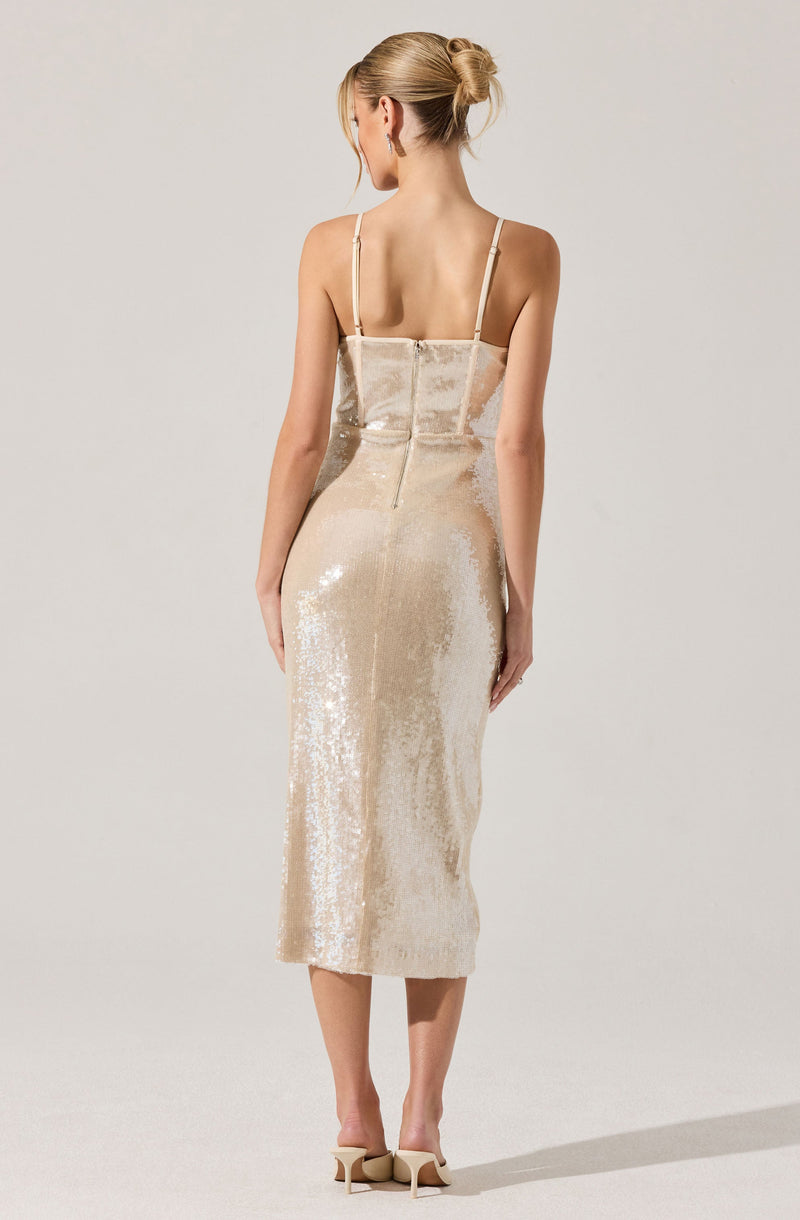 A woman is wearing a long, sequined, champagne-colored dress with thin spaghetti straps. The dress features a fitted bodice with a back zipper, and the fabric has a shiny, reflective quality.