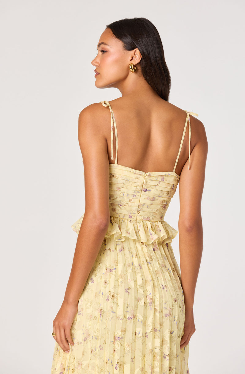 Woman wearing a yellow floral dress with thin shoulder straps and ruffled waist detail.
