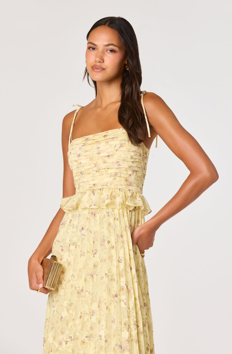 Woman in a yellow floral dress with thin shoulder straps and a ruffled waist.