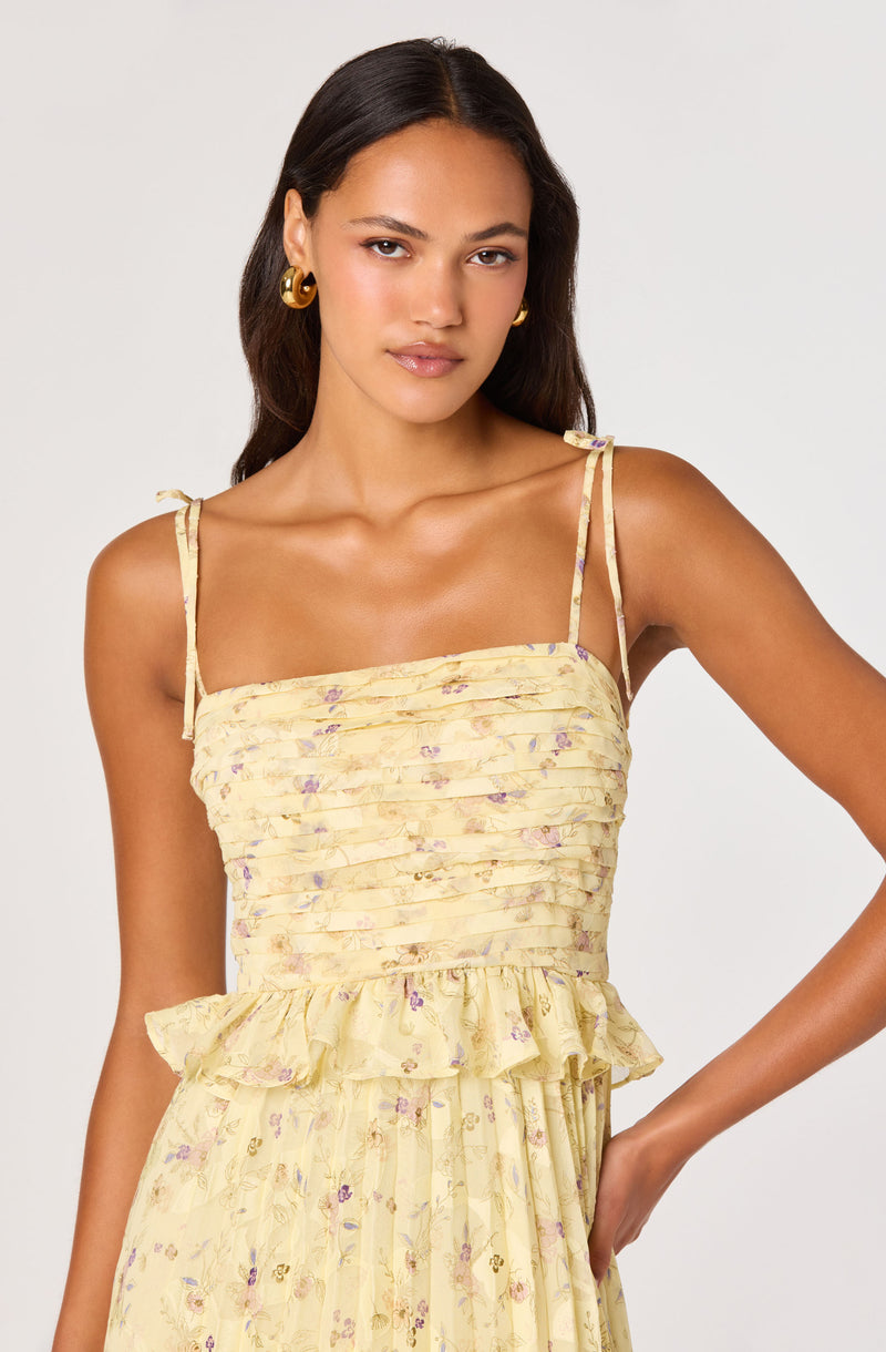 Woman in a yellow floral dress with ruched bodice and ruffled waist, thin shoulder straps.