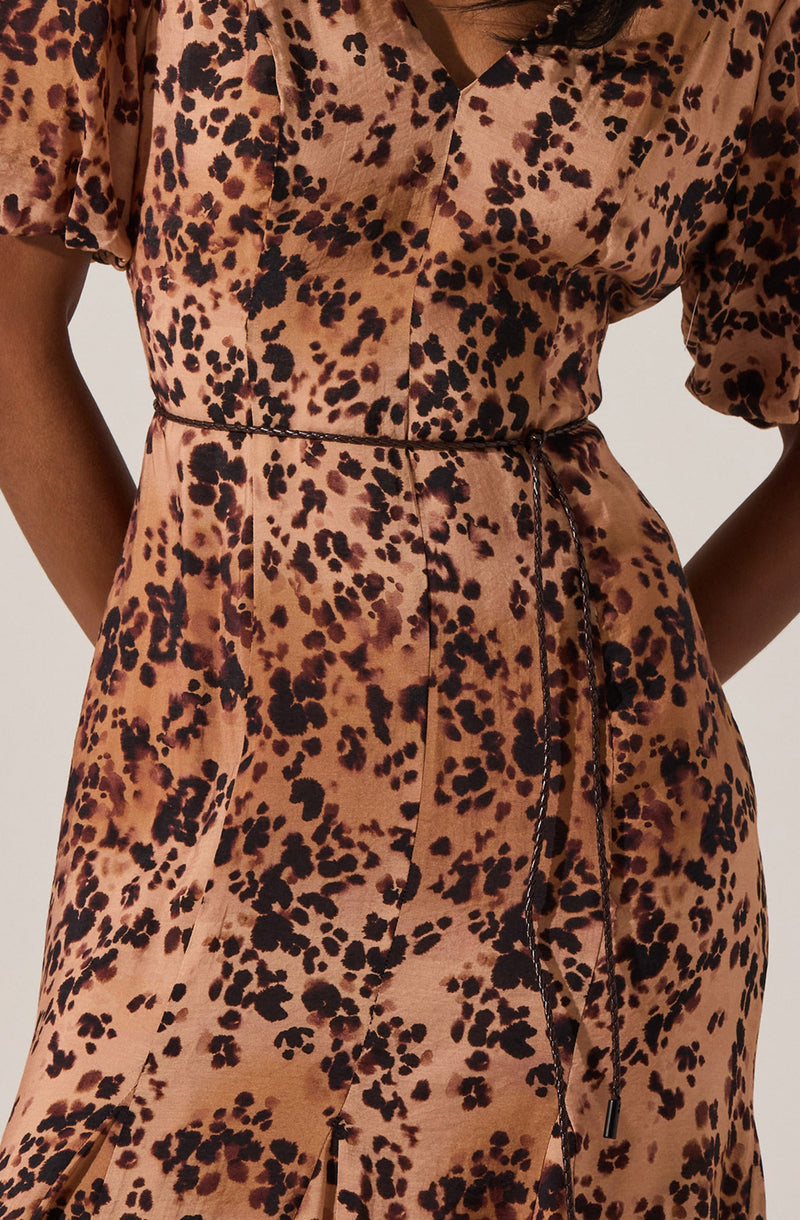 A woman is wearing a matching two-piece outfit made of silky fabric with a leopard print pattern. The top has a V-neckline and short, puffed sleeves. The skirt features a high waist with a drawstring tie at the front.