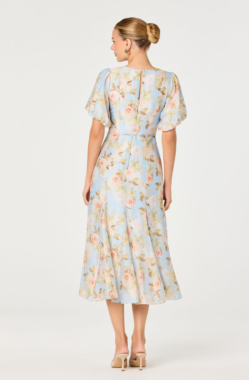 Woman in a floral pastel-colored dress with puffed short sleeves and a midi length.