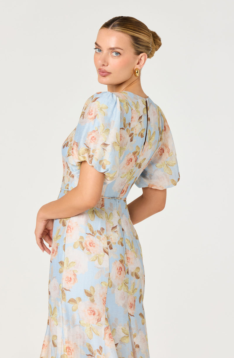 Woman in a pastel blue floral dress with puffed sleeves and a fitted waist.