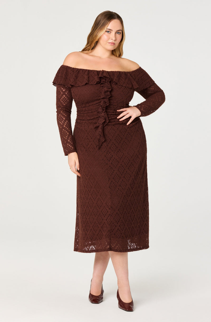 A woman is wearing an off-the-shoulder, long-sleeved, burgundy lace dress with a ruffled neckline and ruffle detail running down the front. The dress is fitted at the waist and extends to mid-calf length. She is also wearing matching burgundy heels.