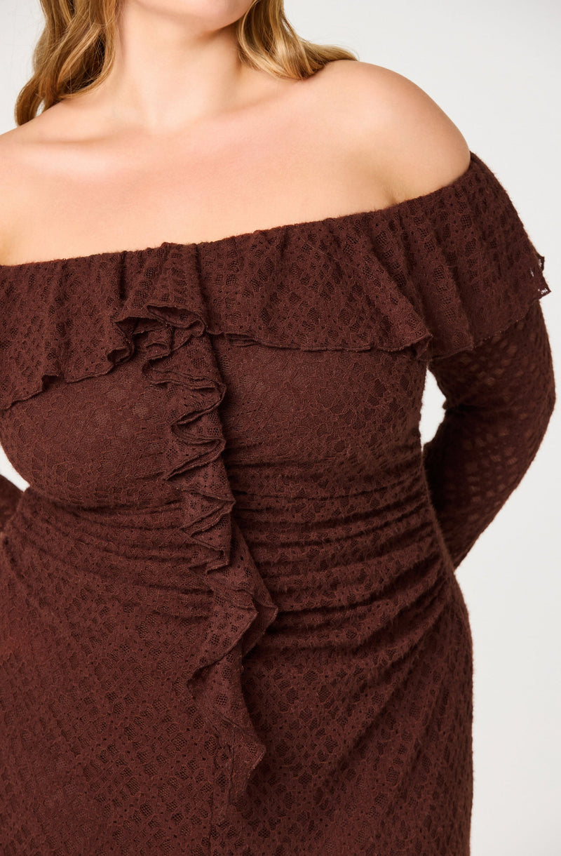 A woman is wearing a maroon off-the-shoulder dress with ruffled details along the neckline and down the front. The dress has a textured pattern, and the long sleeves are fitted, matching the dress fabric.