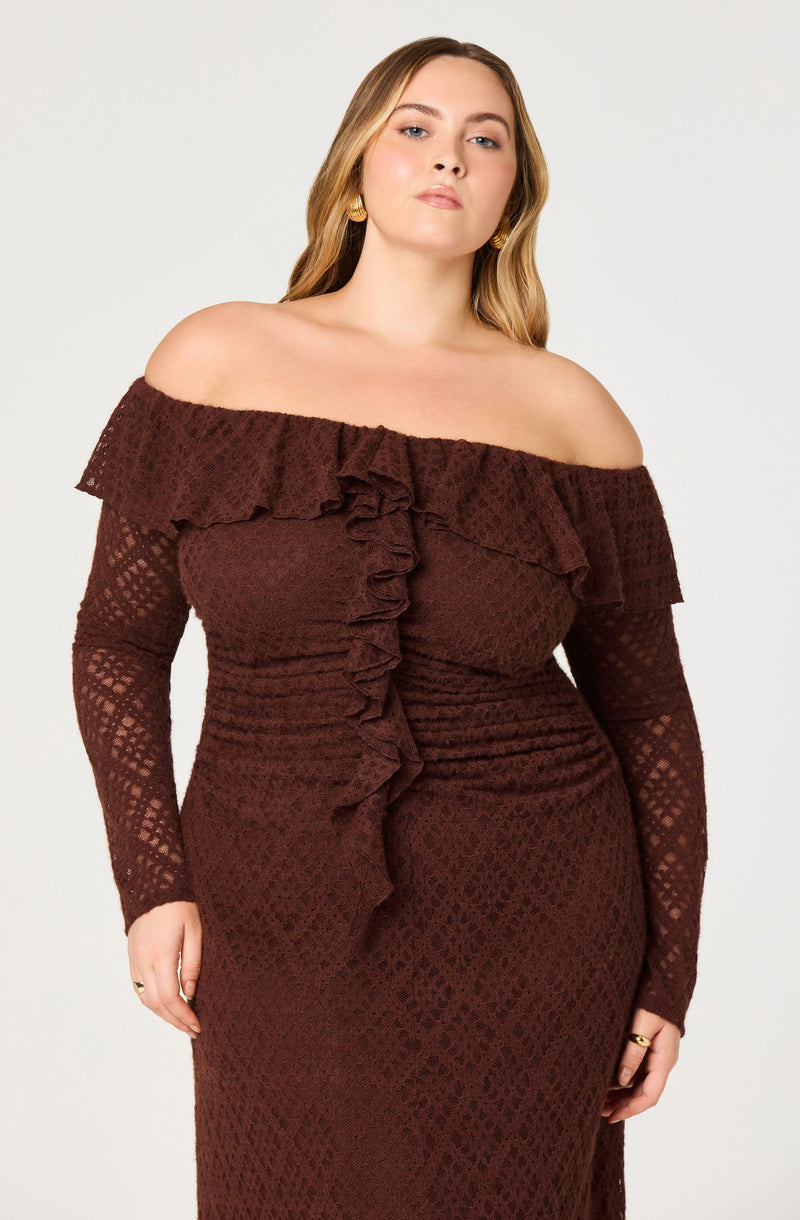 A woman is wearing a fitted, off-the-shoulder dress with long sleeves. The dress features a ruffled neckline that drapes over the shoulders and extends down the front, with a textured, lace-like pattern throughout. The fabric is a deep, rich brown color.