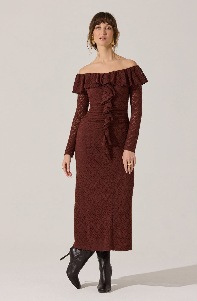 A woman is wearing a long, off-the-shoulder dress in a deep burgundy color with a ruffled neckline. The dress features a textured pattern, long lace sleeves, and a ruffle detail running down the front. She has paired the dress with black, heeled boots.
