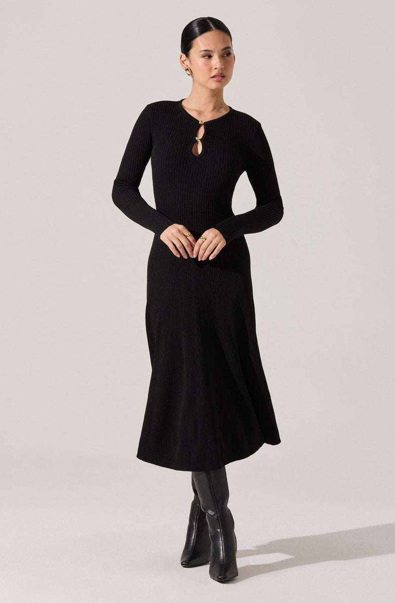 A woman is wearing a long black ribbed knit dress with long sleeves. The dress features a small keyhole opening at the neckline, secured with a round button. She completes the look with black knee-high boots.