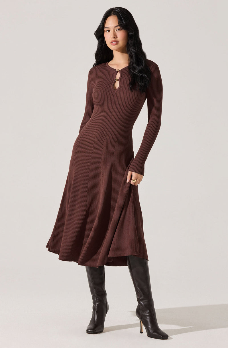 A woman is wearing a long, ribbed, brown dress with a fitted bodice, long sleeves, and a flared skirt. The dress features a small keyhole opening at the neckline, held together with two decorative circular clasps.