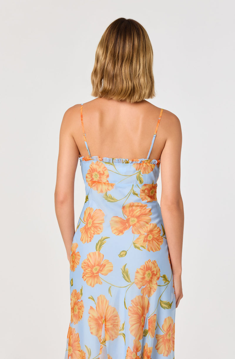Back view of a woman wearing a light blue, floral print dress with orange flowers and thin straps.