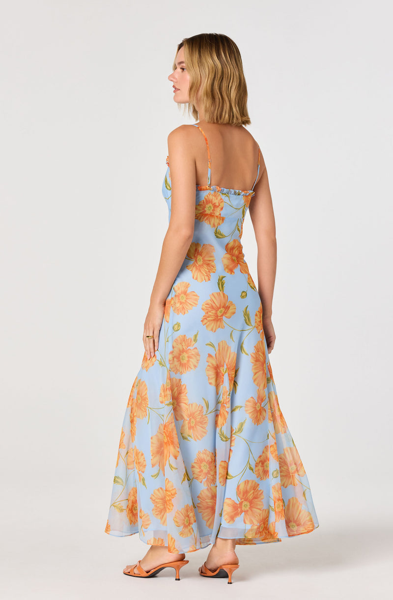 Woman in a long, blue floral dress with orange flowers and thin shoulder straps.