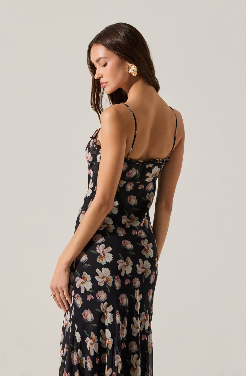 A woman is wearing a black sleeveless dress with thin, adjustable spaghetti straps. The dress features a floral pattern with large white, pink, and peach-colored flowers with green leaves. The fabric appears lightweight and flowy.