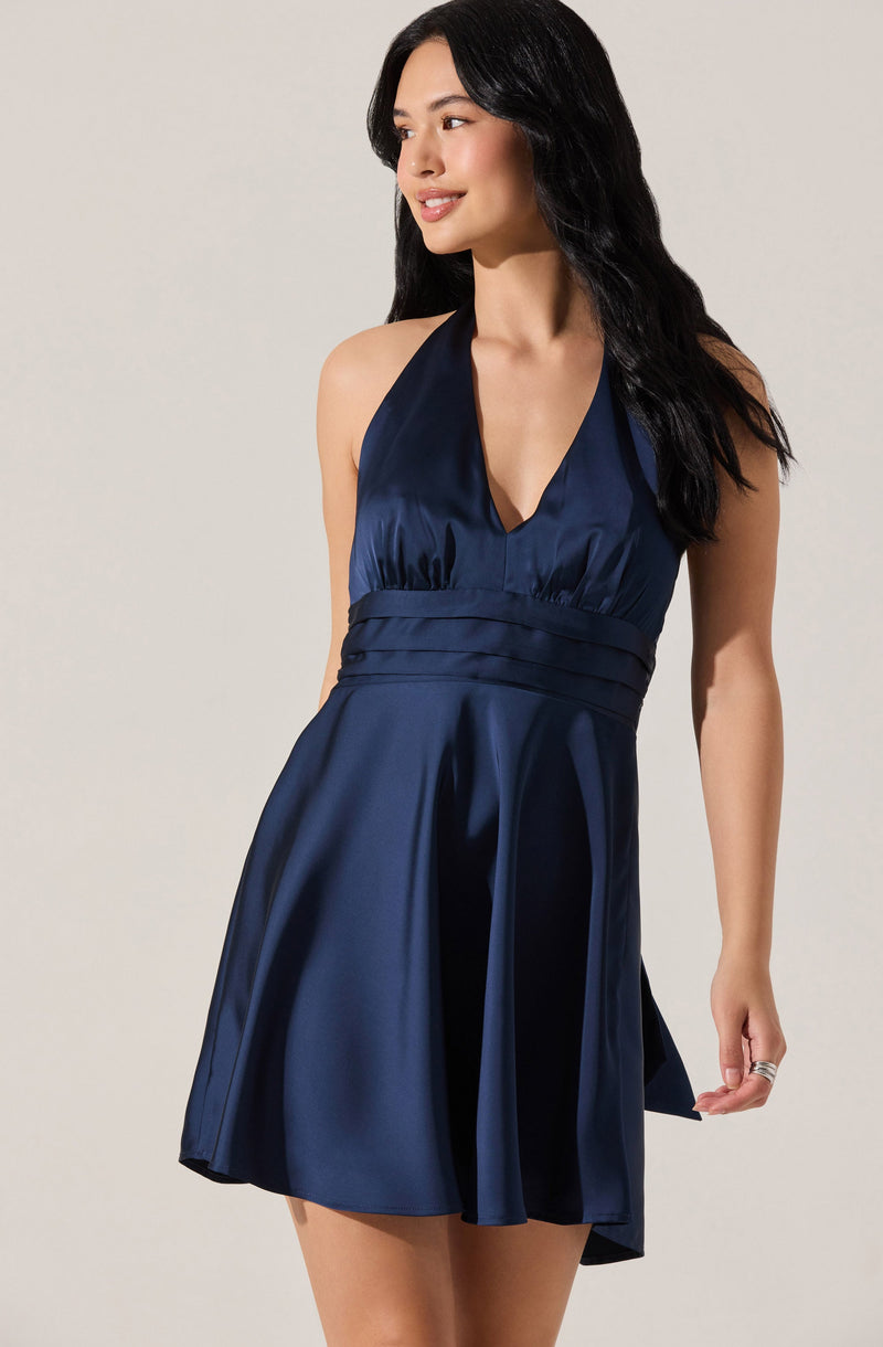A woman is wearing a sleeveless, deep navy blue satin dress with a halter neckline. The dress features a fitted bodice with gathered details at the waist and a flared skirt that falls above the knees. The shiny satin fabric adds a smooth, luxurious appearance.