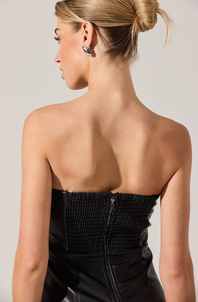 A woman with her hair in a bun is wearing a strapless black top with a textured, smocked front and a visible zipper at the back.