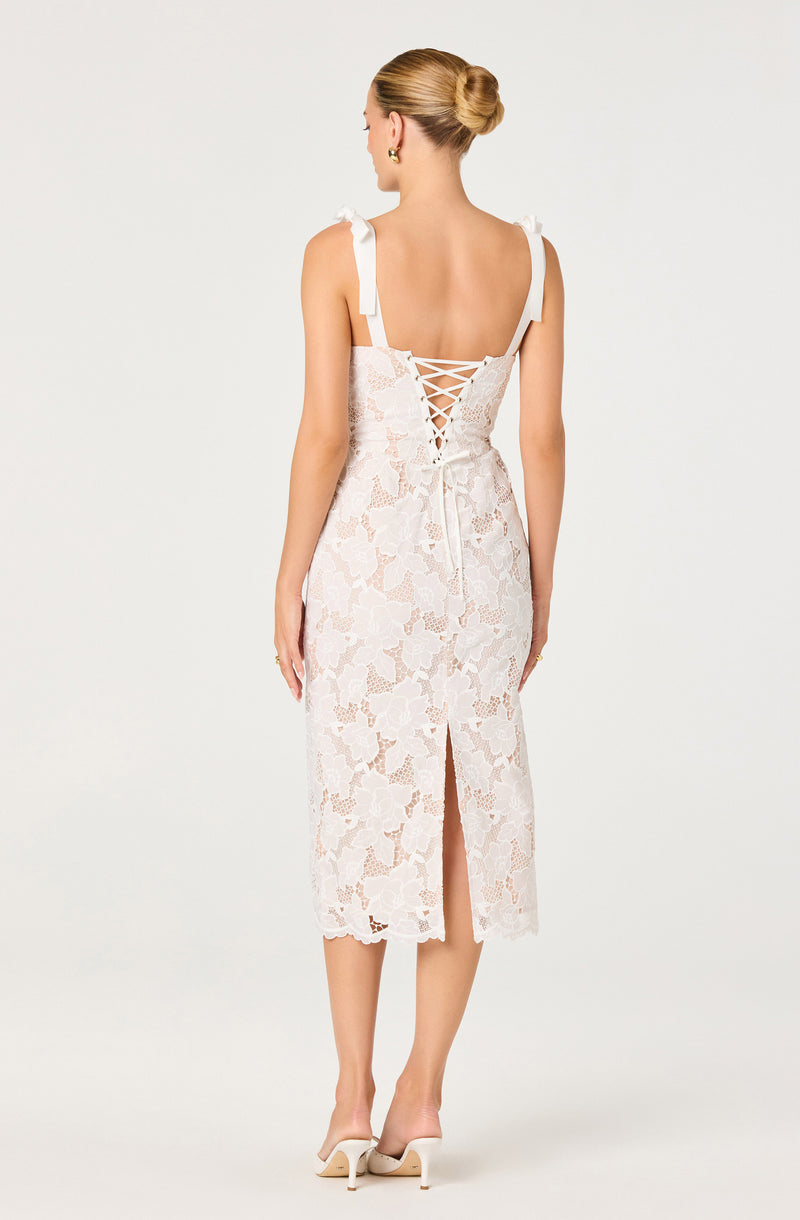 White lace dress with bow shoulder straps and a lace-up back detail.