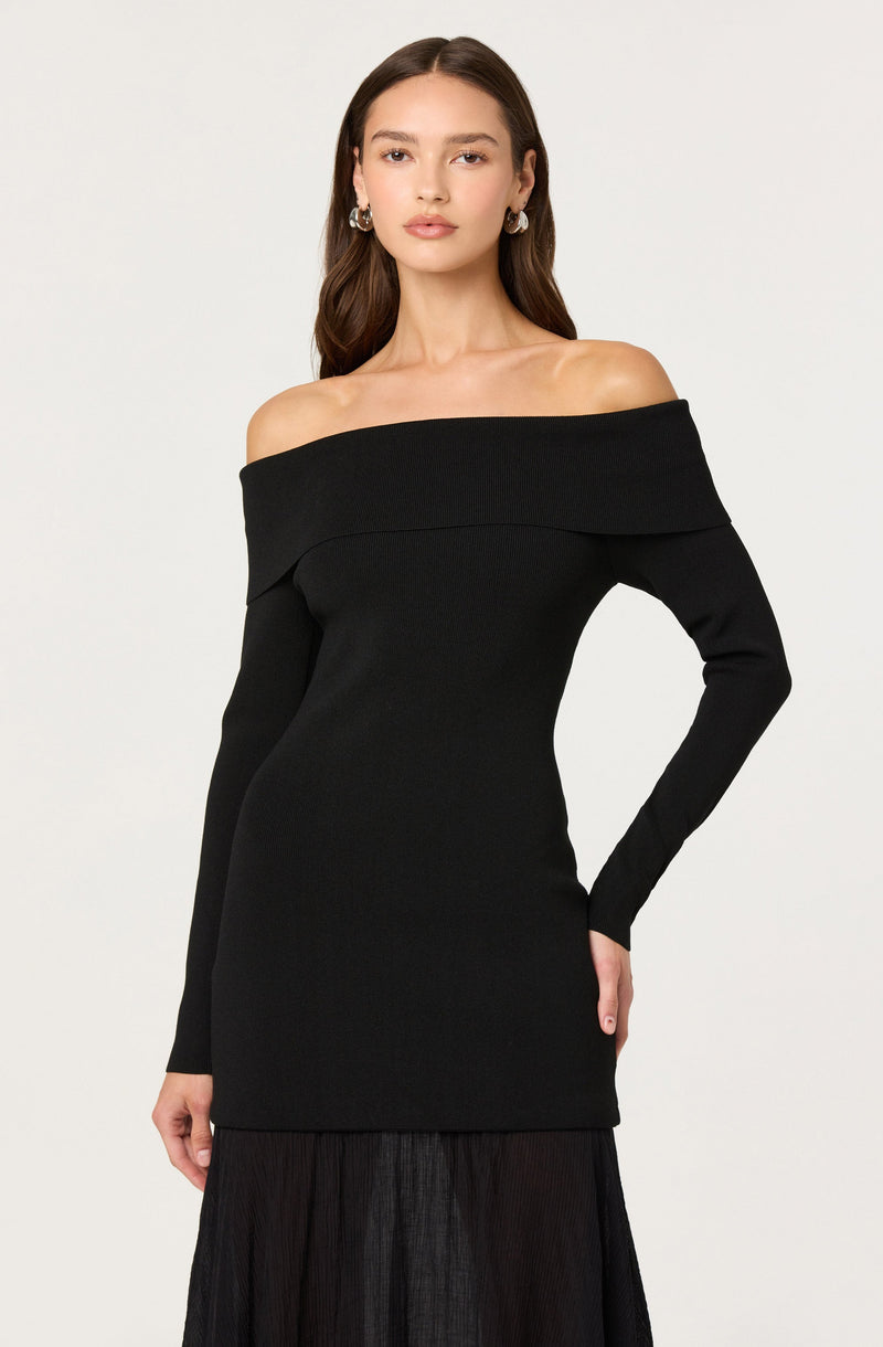 A woman is wearing an off-the-shoulder black dress with long sleeves and a fitted silhouette. The dress features a wide neckline that exposes her shoulders and collarbone.