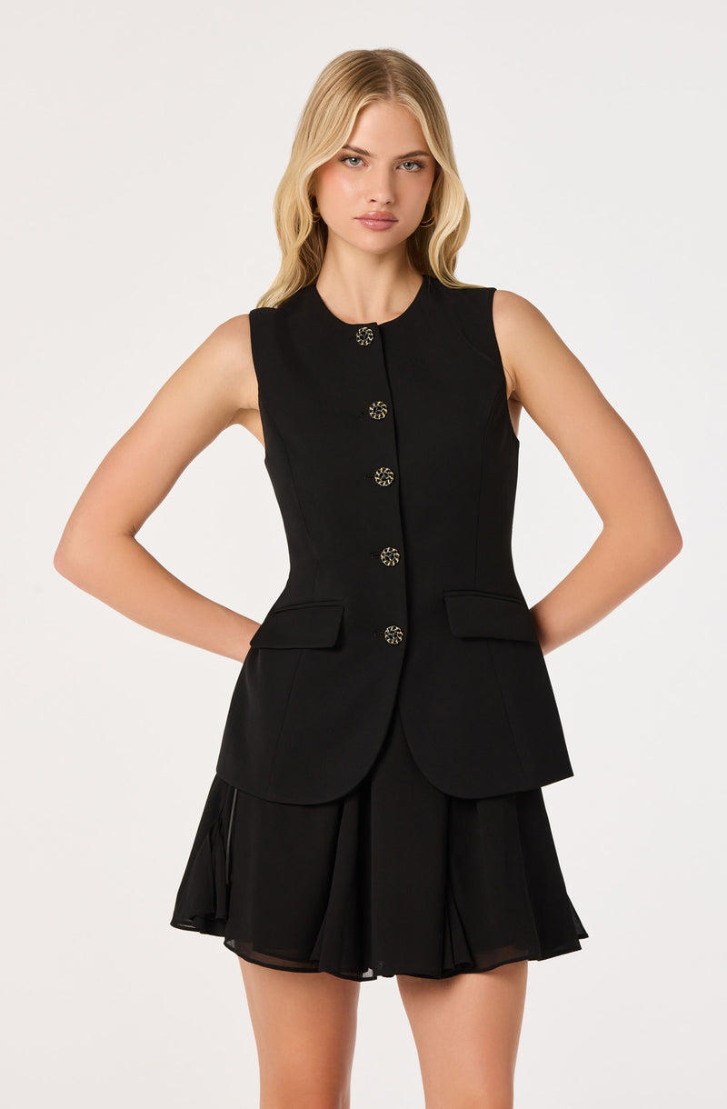 Black sleeveless blazer with gold buttons and a matching black pleated skirt.