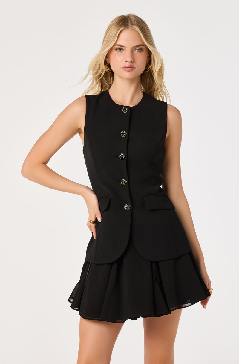 Woman in sleeveless black vest with gold buttons and matching black skirt with ruffles.