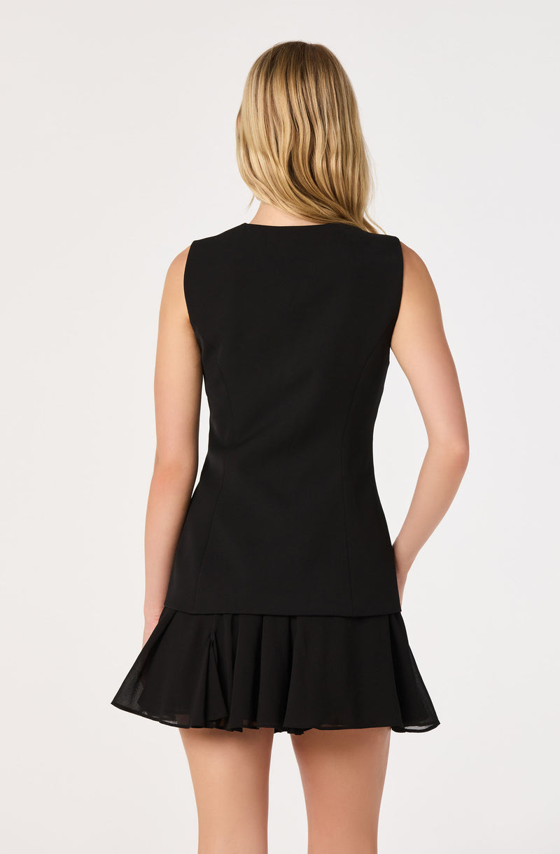 Woman wearing a sleeveless black top with a fitted waist and a short, pleated black skirt.
