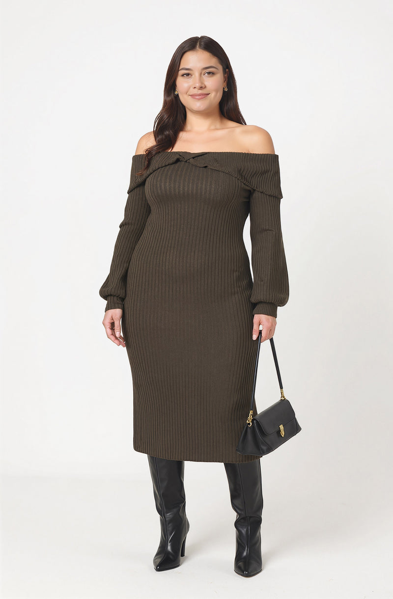 A woman is wearing an off-the-shoulder, long-sleeve, ribbed knit dress in a dark olive green color. The dress has a fitted silhouette that extends below the knees. She is also carrying a small black handbag with a gold clasp and wearing black knee-high boots made of shiny material.