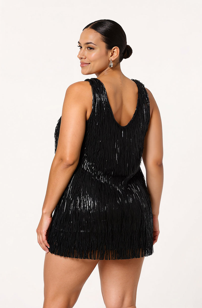 A woman is wearing a sleeveless black dress made of shiny, textured fringe material. The dress has a deep V neckline in the back and reaches mid-thigh length.