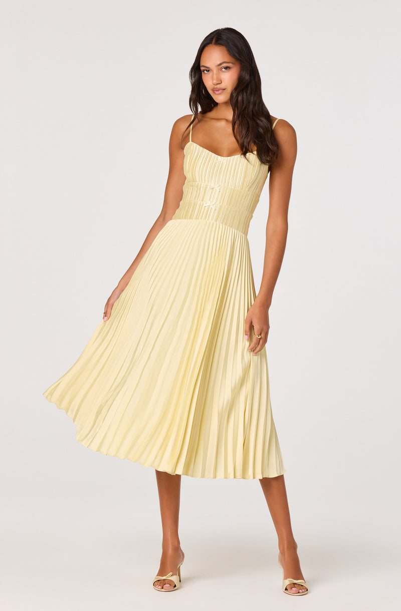 Woman in a yellow pleated midi dress with spaghetti straps and beige heels.