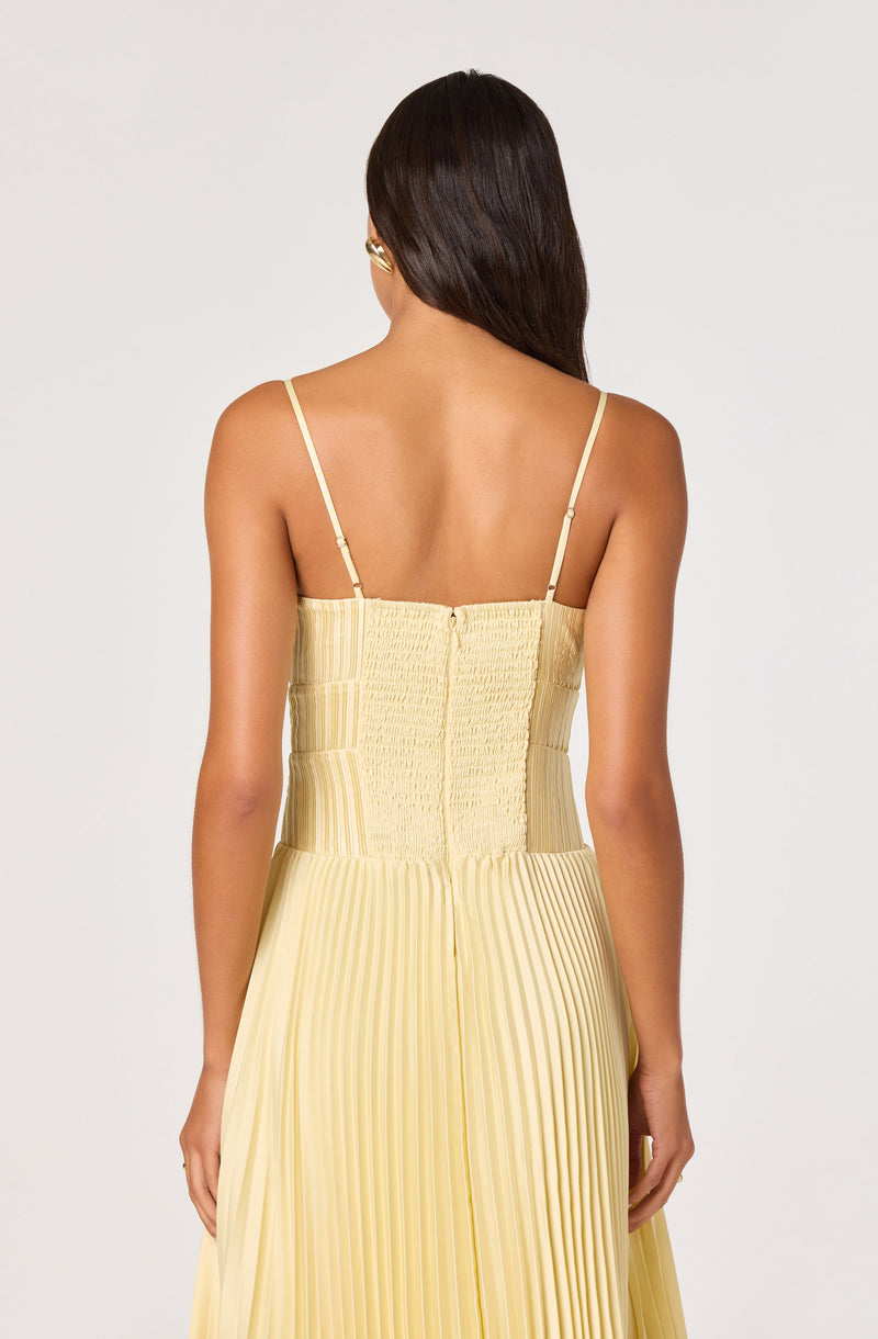 Back view of a woman in a yellow pleated dress with thin spaghetti straps.
