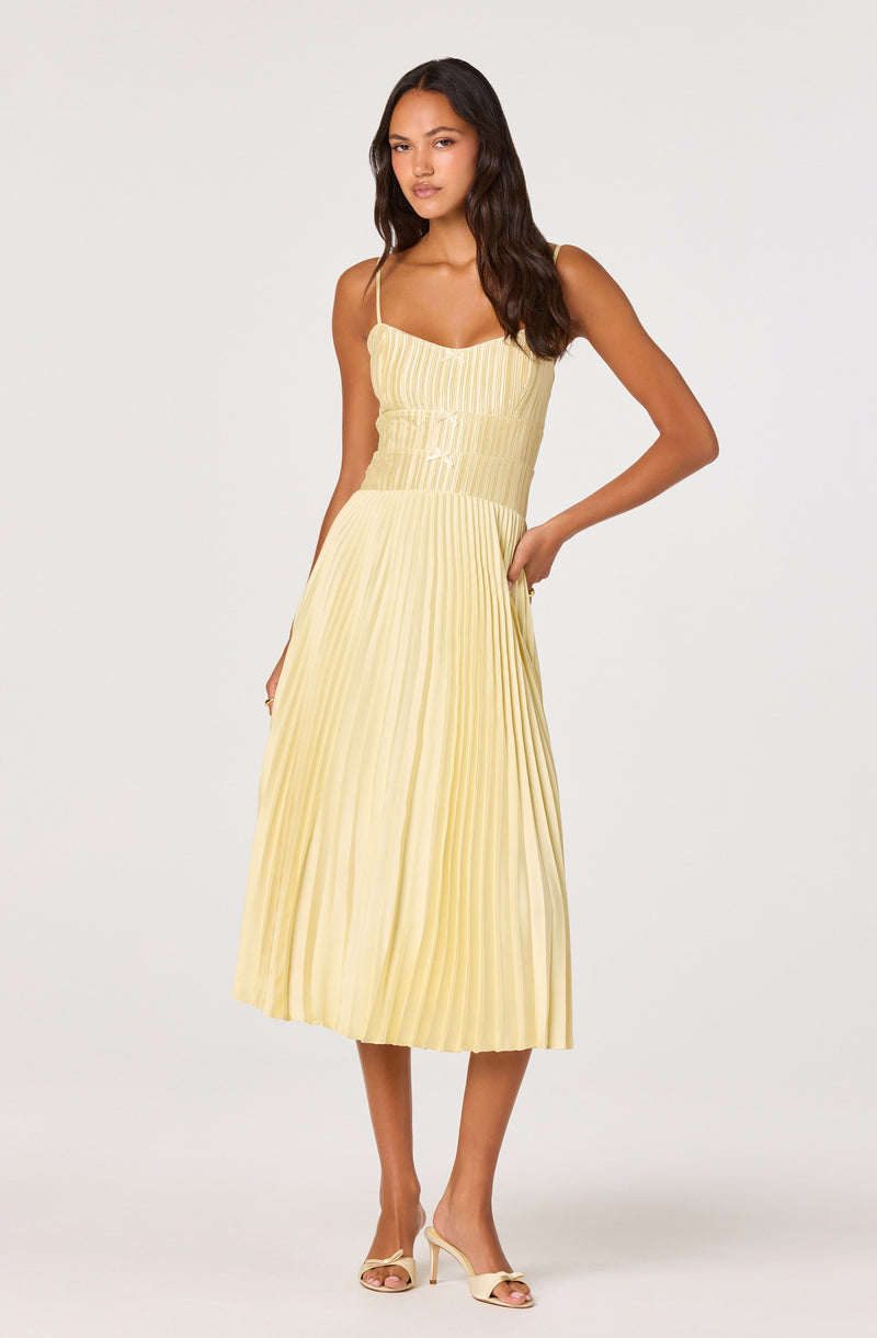 Woman wearing a yellow sleeveless pleated midi dress with spaghetti straps.