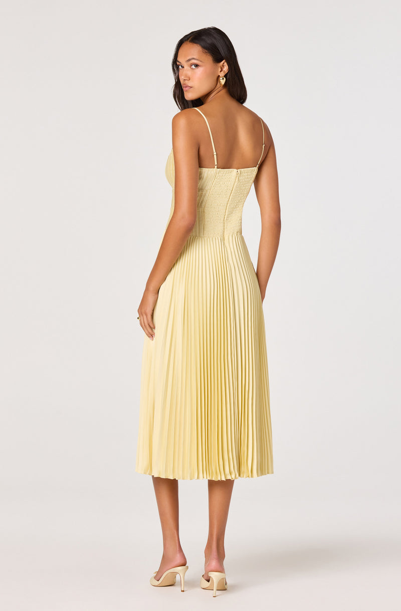 Woman in a yellow pleated midi dress with spaghetti straps and beige high-heeled shoes.