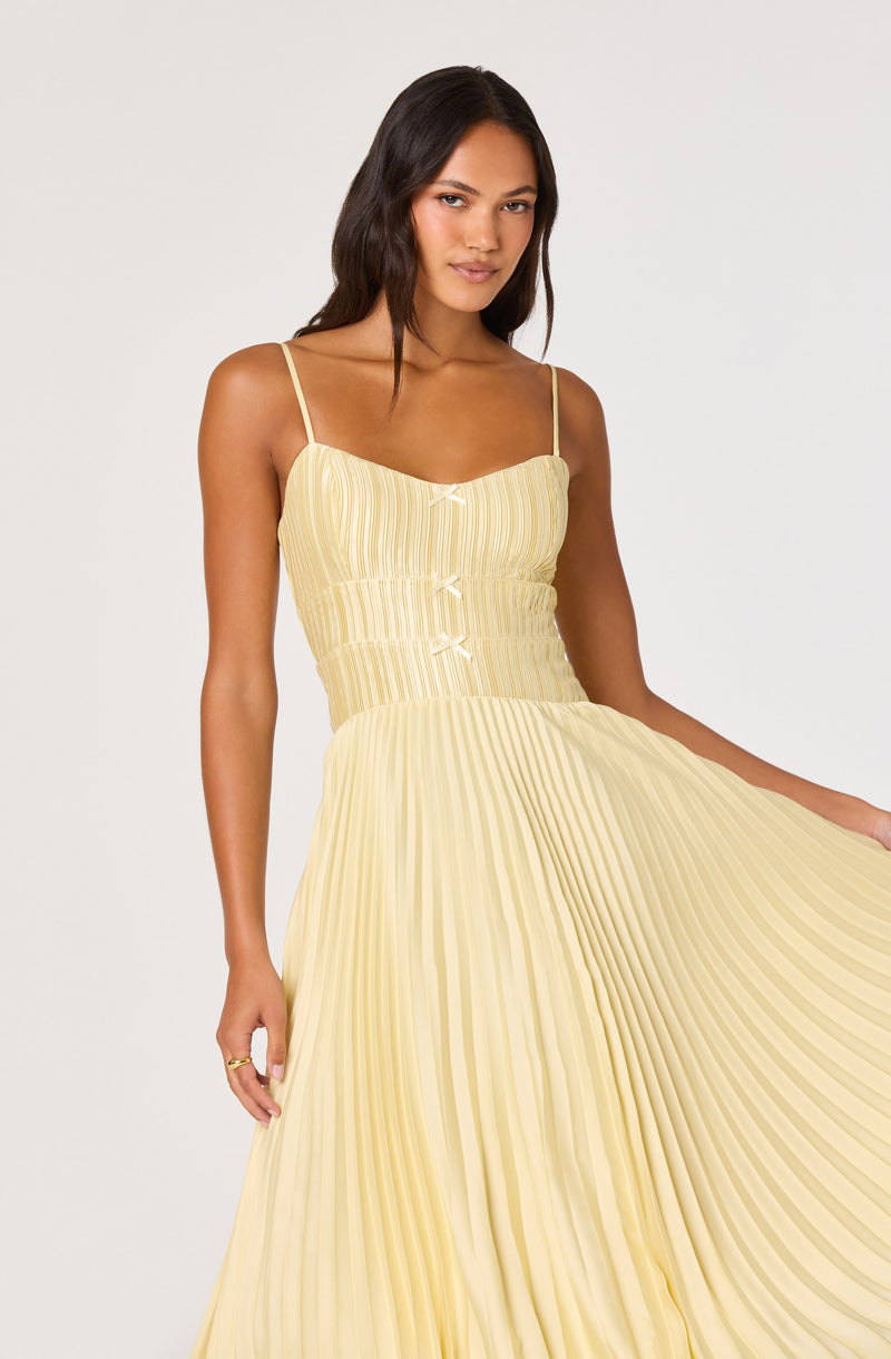 Woman in a yellow pleated dress with thin spaghetti straps and a fitted bodice.
