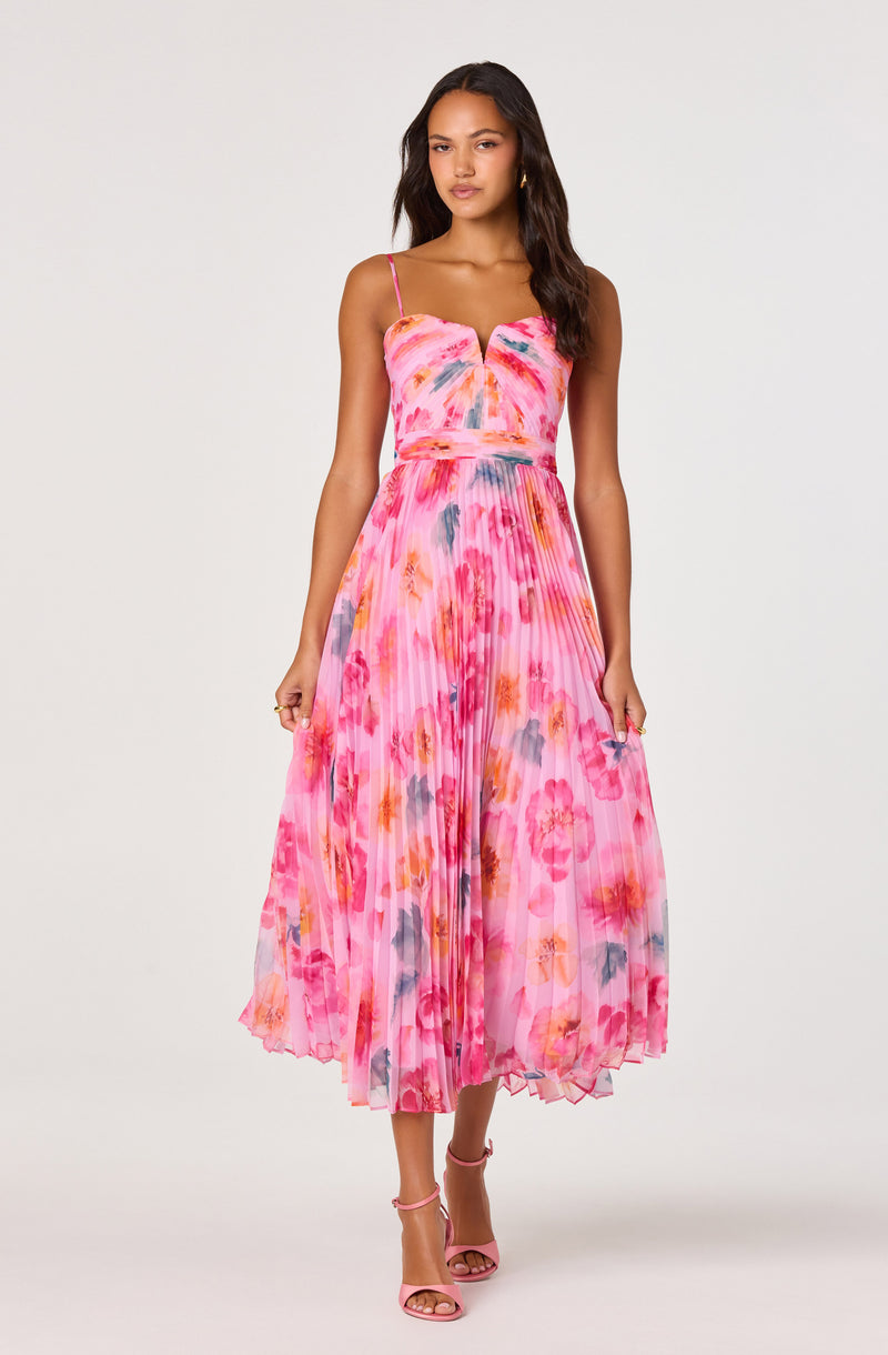 Woman wearing a pink floral pleated dress with spaghetti straps and open-toe heels.