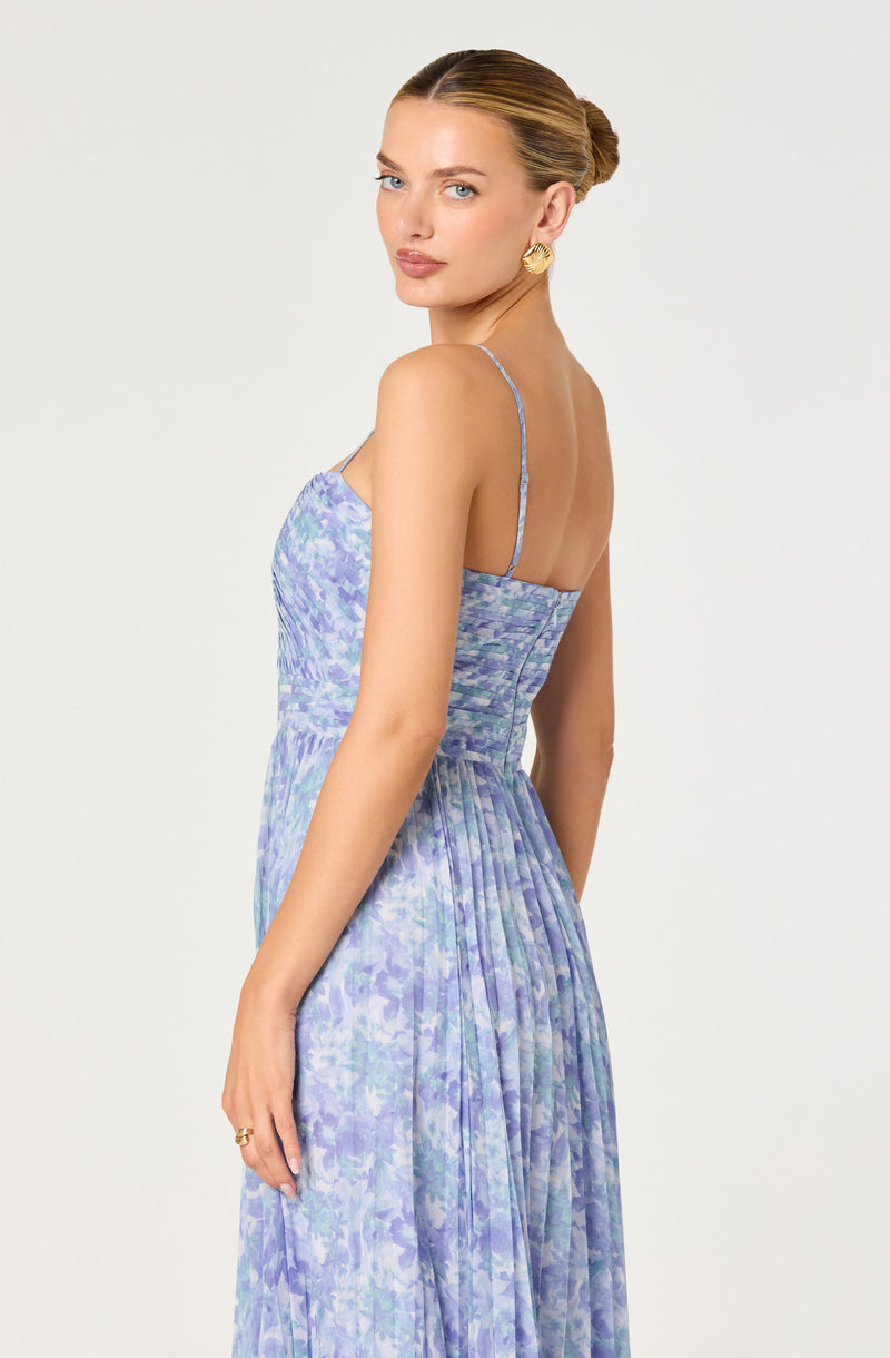 Woman in a blue floral dress with thin straps, fitted bodice, and pleated skirt.