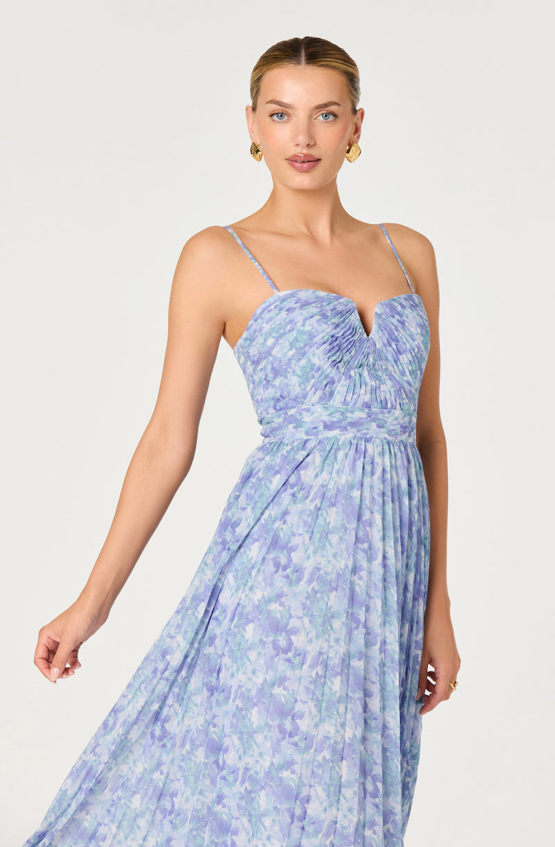 Woman in a sleeveless, purple and blue patterned spaghetti strap dress with ruching at the bust.
