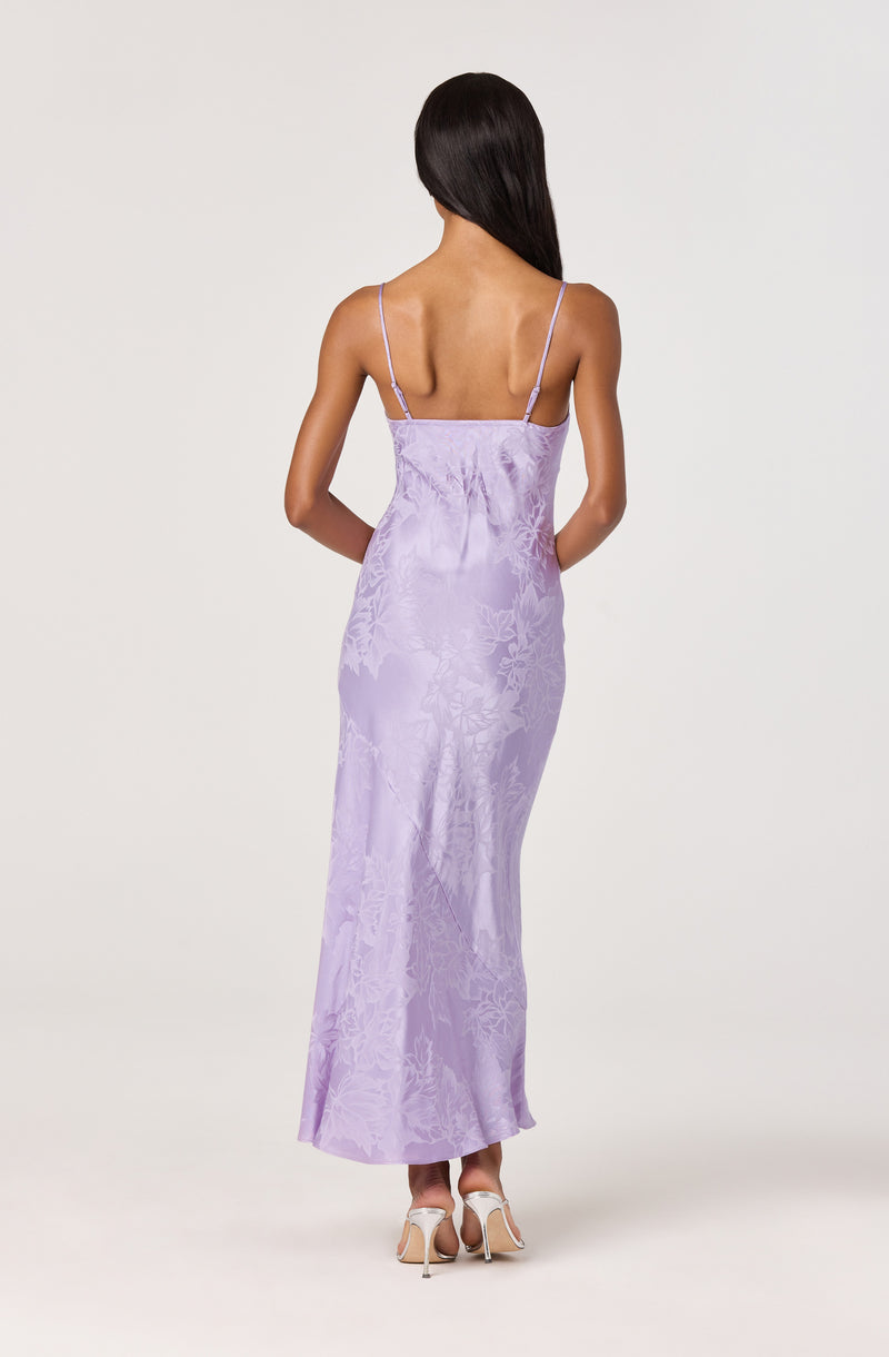 Woman in a long, lavender, patterned satin dress with spaghetti straps, viewed from the back.