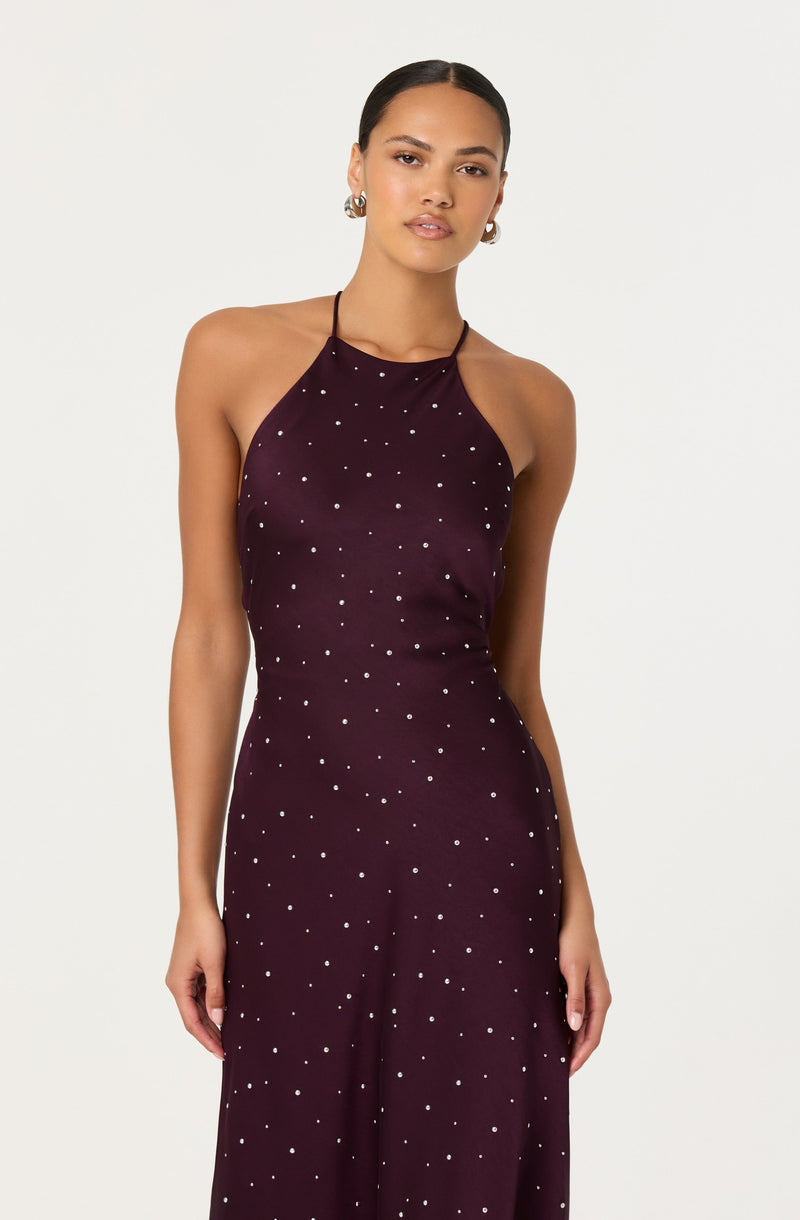 A woman is wearing a sleeveless, halter-neck dress in a dark purple or burgundy color. The dress features a pattern of small white polka dots evenly distributed across the fabric.
