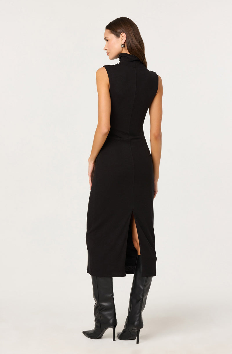 A woman is wearing a sleeveless black dress with a high neckline and a slit at the back that reveals part of her legs. She is also wearing black thigh-high leather boots with pointed toes and stiletto heels.
