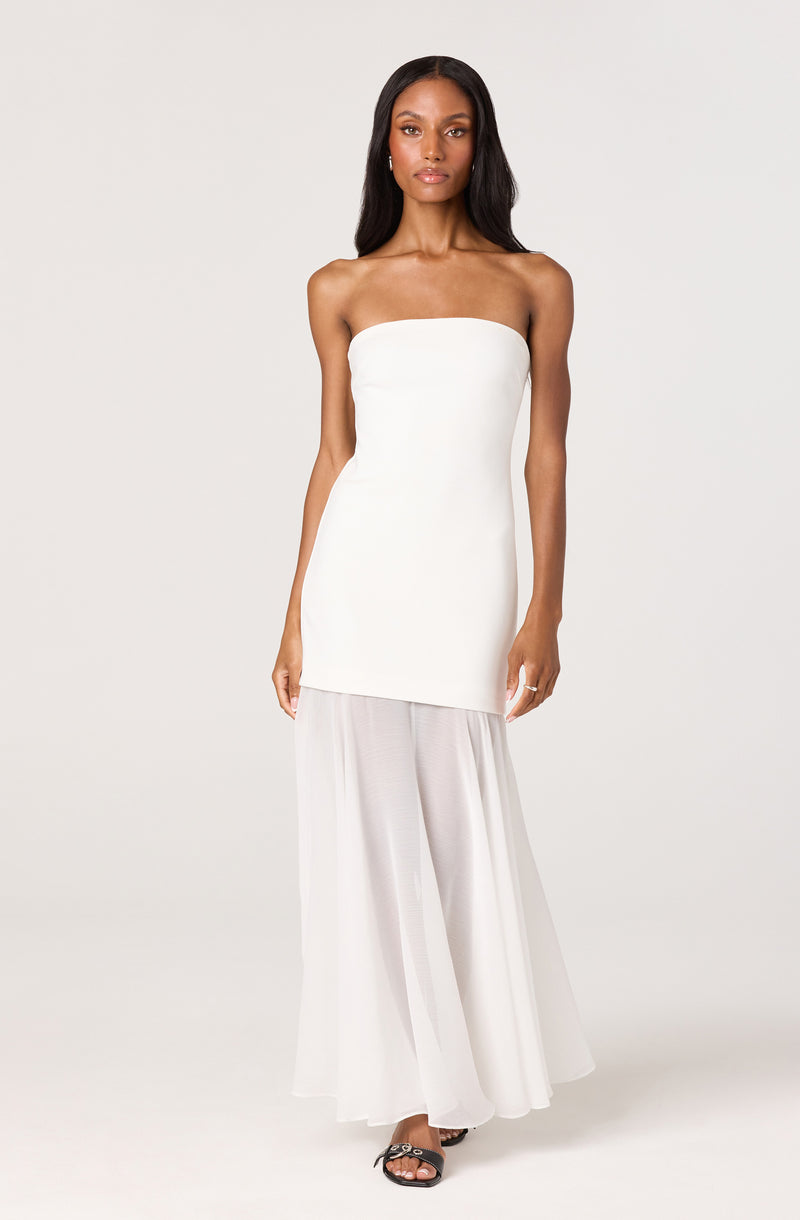 Woman in a strapless white top and wide-leg white pants with black sandals.