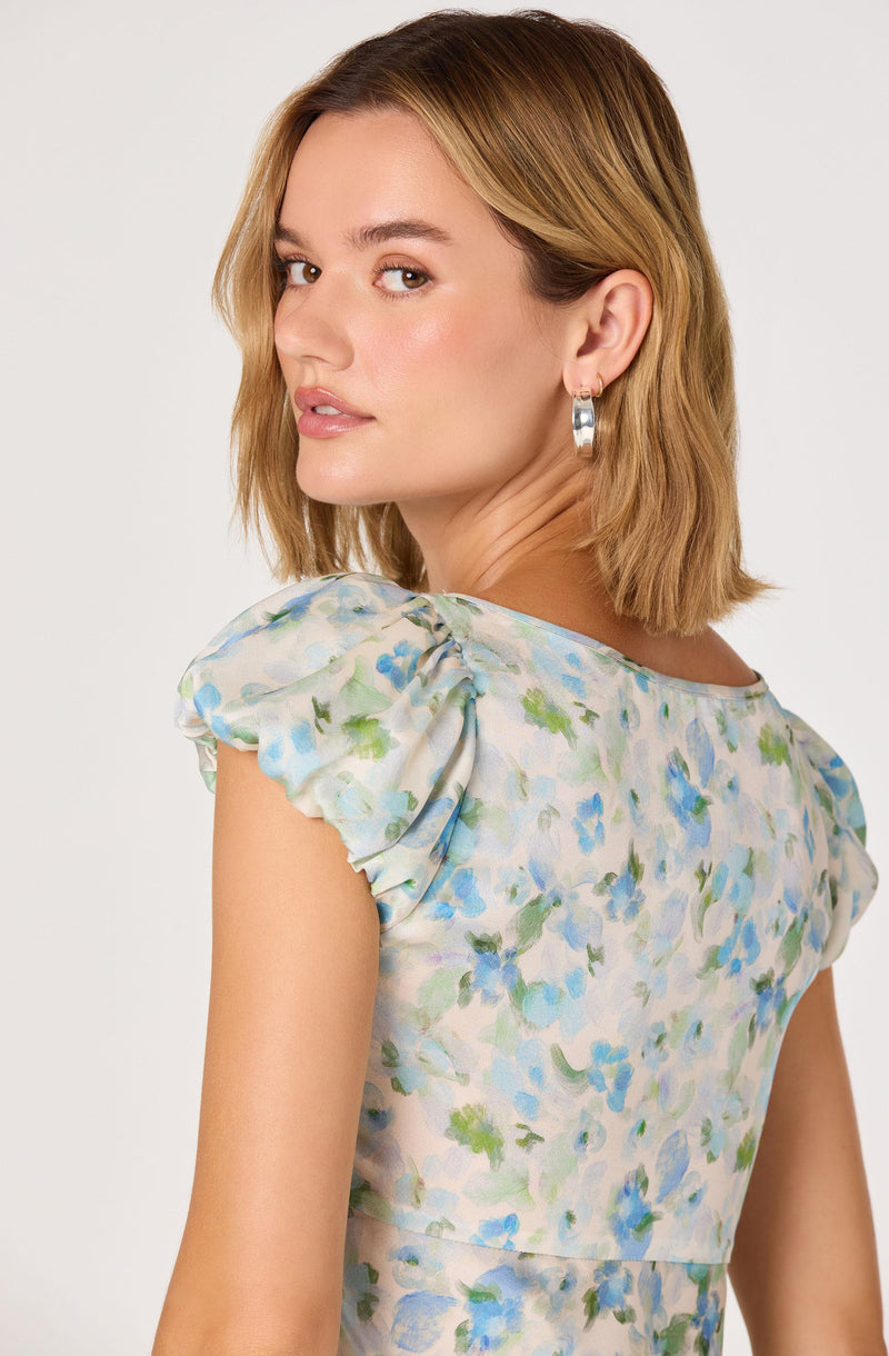 Woman wearing a light floral dress with puffed sleeves, in soft pastel colors.