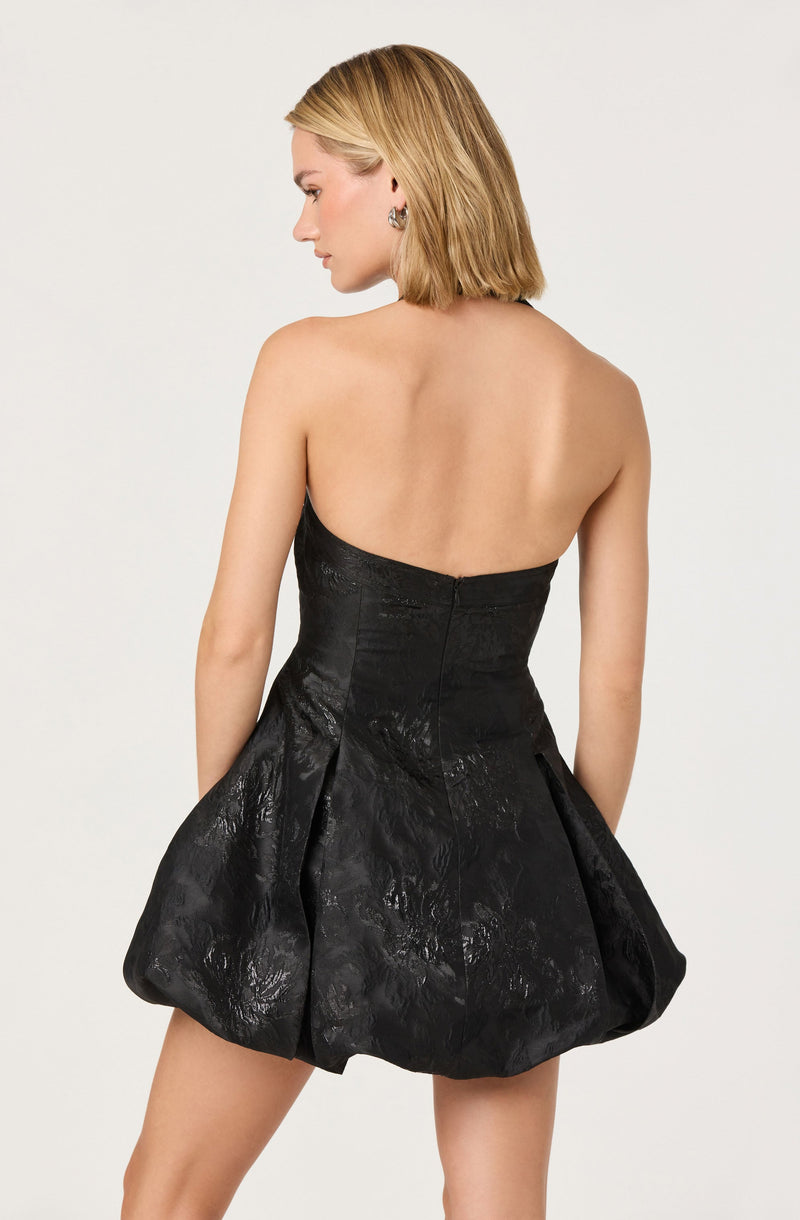A woman is wearing a strapless black dress with a fitted bodice and a voluminous, textured skirt that has a shiny, reflective surface.