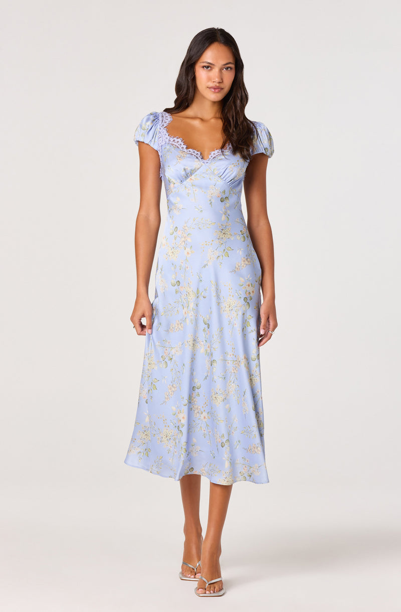 Woman wearing a light blue floral dress with puff sleeves and lace details at the neckline.