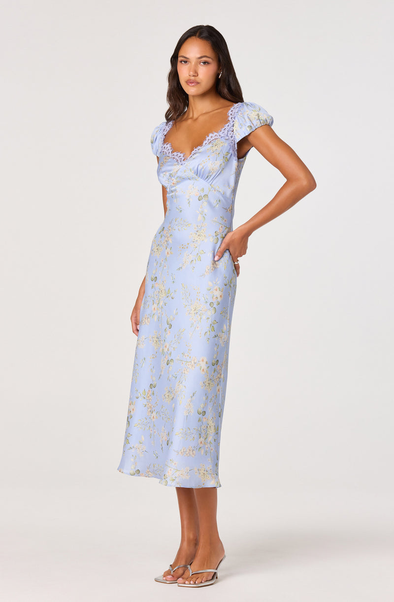 Woman in a light blue dress with gold floral pattern, lace details on the neckline and puff sleeves.
