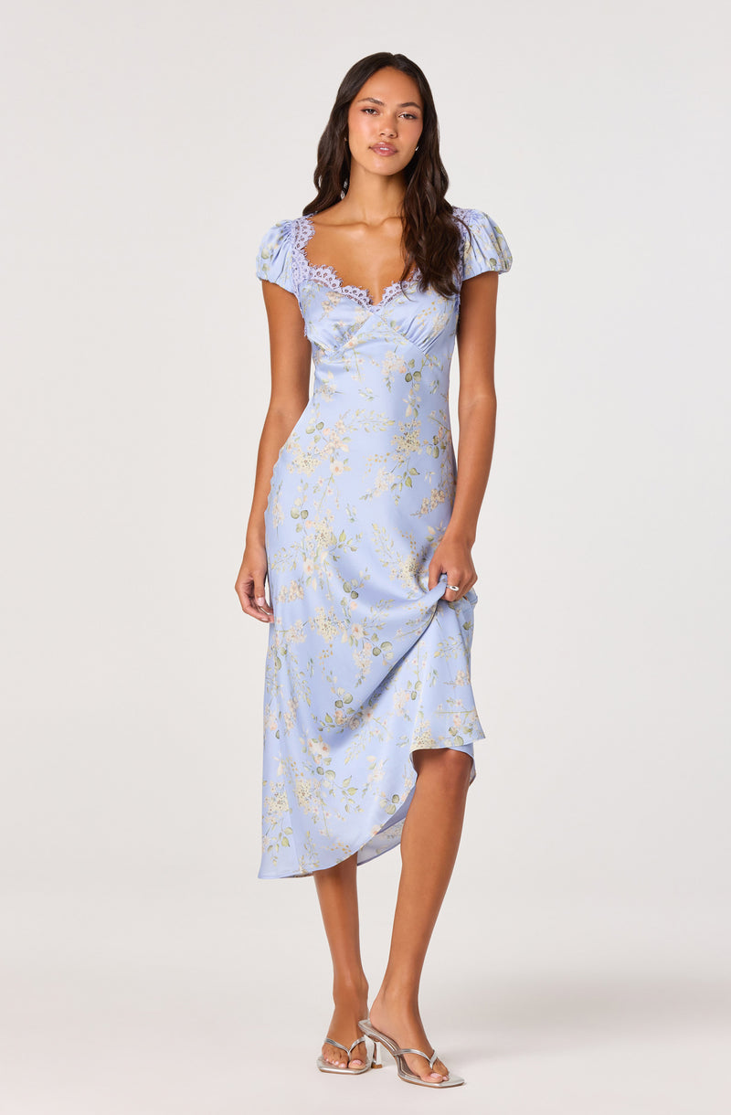 Woman wearing a light blue floral dress with puffed short sleeves and lace trim at the neckline.